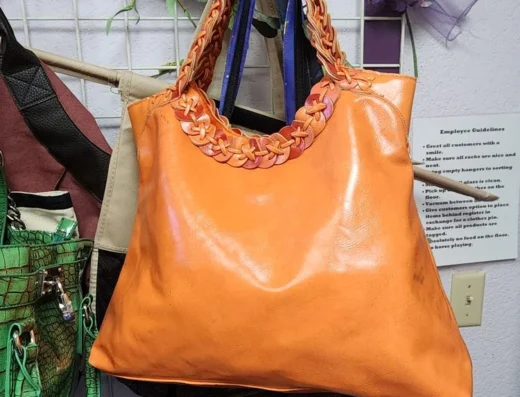 Orange leather tote bag with braided handles hanging on a display rack.