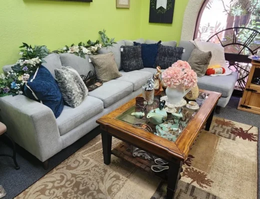 L-shaped gray sofa with many cushions in a bright lime-green living room, centered by a wooden coffee table with a glass top and floral centerpiece.