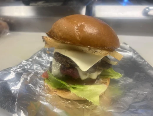 Close up of a cheeseburger with a toasted bun melted cheese beef patty lettuce and tomato on foil wrapped foil