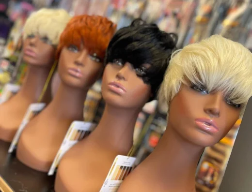 Three mannequin heads wearing short wigs in blonde, copper, and black sit on a display shelf in a wig shop window/aisle shelf.
