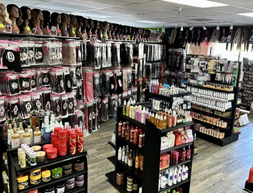 Beauty supply store aisle with racks of wigs and hair extensions displayed on top shelves, plus shelves of hair care products below the mannequins.