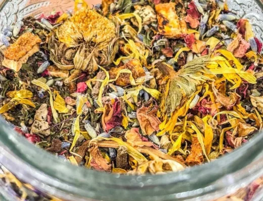 Loose herbal tea blend with yellow petals and dried leaves in a glass jar.