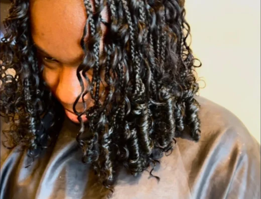 Person with wet twisted dreadlocks looking downward, wearing a dark drape-like shirt.