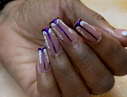 Close-up of hands displaying purple and white nail art with vertical purple stripes and white petal shapes; beaded bracelet in background.