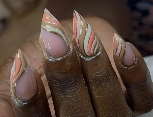 Close-up of five almond-shaped nails with swirling pink, coral, gray, and gold striped nail art on dark skin, glossy finish.