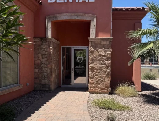 Dental clinic entrance with a peach stucco building and stone columns, glass door, and a large 'DENTAL' sign above the doorway on a sunny day
