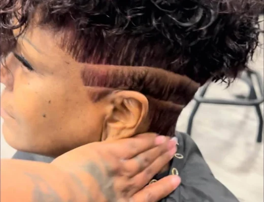 Close-up of a person with short, curly dark hair being held by a tattooed hand around their neck.