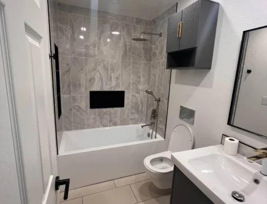 Modern bathroom with gray tiled shower white tub wall cabinet toilet and white vanity