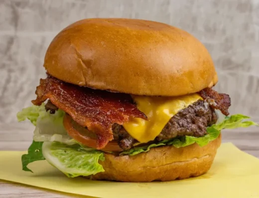 Juicy bacon cheeseburger with cheddar, lettuce, and tomato on a toasted brioche bun on a yellow napkin.