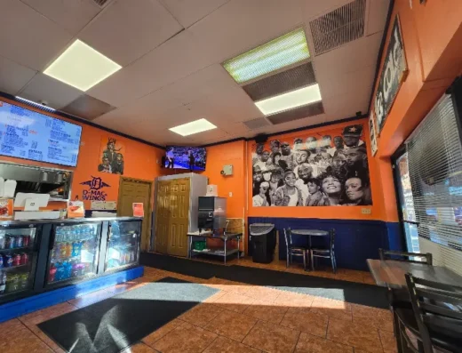 Interior of a fast-food restaurant with orange walls, a counter with a beverage cooler, menu boards, a black-and-white crowd mural, and seating by the window.
