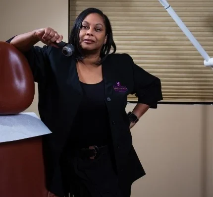 Professional clinician in a black blazer leaning on a dental chair in a treatment room with an overhead light above