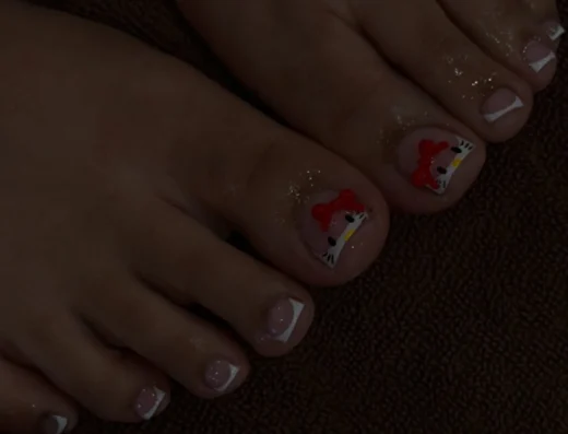 Pedicured toes resting on fabric with white French tips; big toe features a red bow design.