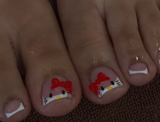 Pedicure on toes featuring Hello Kitty nail art with red bows and white whiskers on pink nails.