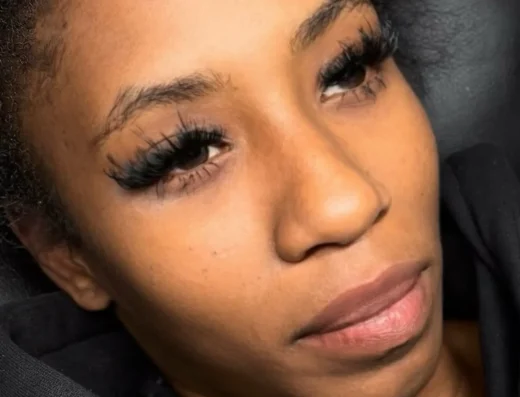 Close-up of a woman with long eyelash extensions and subtle makeup, looking to the left.