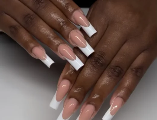 Close-up of hands showing a French manicure with long square white-tipped nails and a nude base on dark skin. -