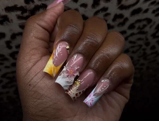 Long coffin shaped nails with pink base and colorful floral nail art on one hand held against a leopard pattern background showing intricate 3D flowers and white swirls
