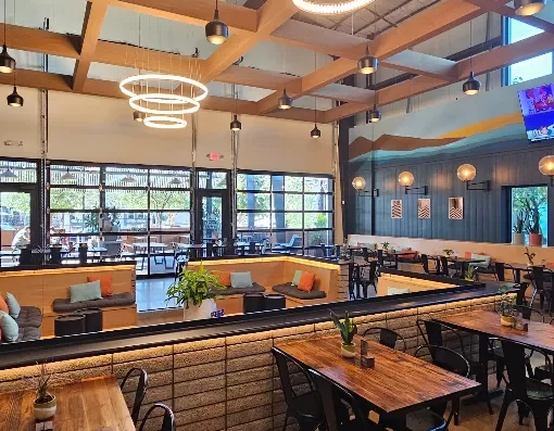 Cozy modern cafe interior with wooden beams, circular pendant lights, and mixed seating. - Open dining area featuring booths along a low brick divider and wooden tables.