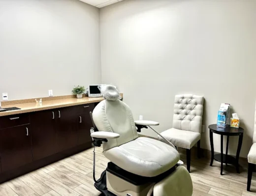 Dental chair in a clean clinic room with beige upholstery, a small monitor, and a countertop along the wall.